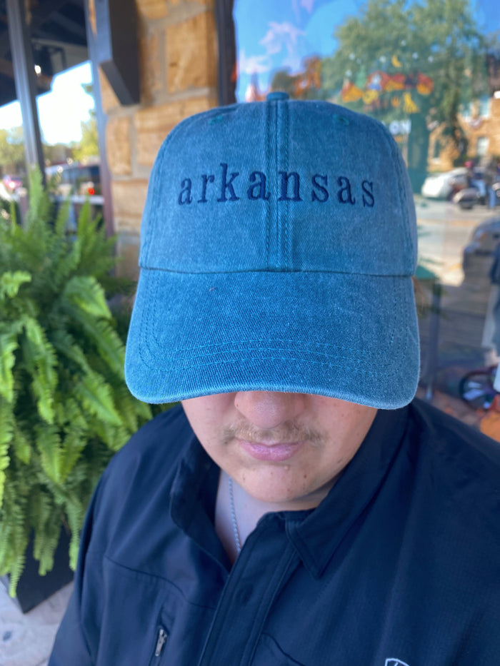blue jean embroidered Arkansas cap being worn outside in front of a green fern plant