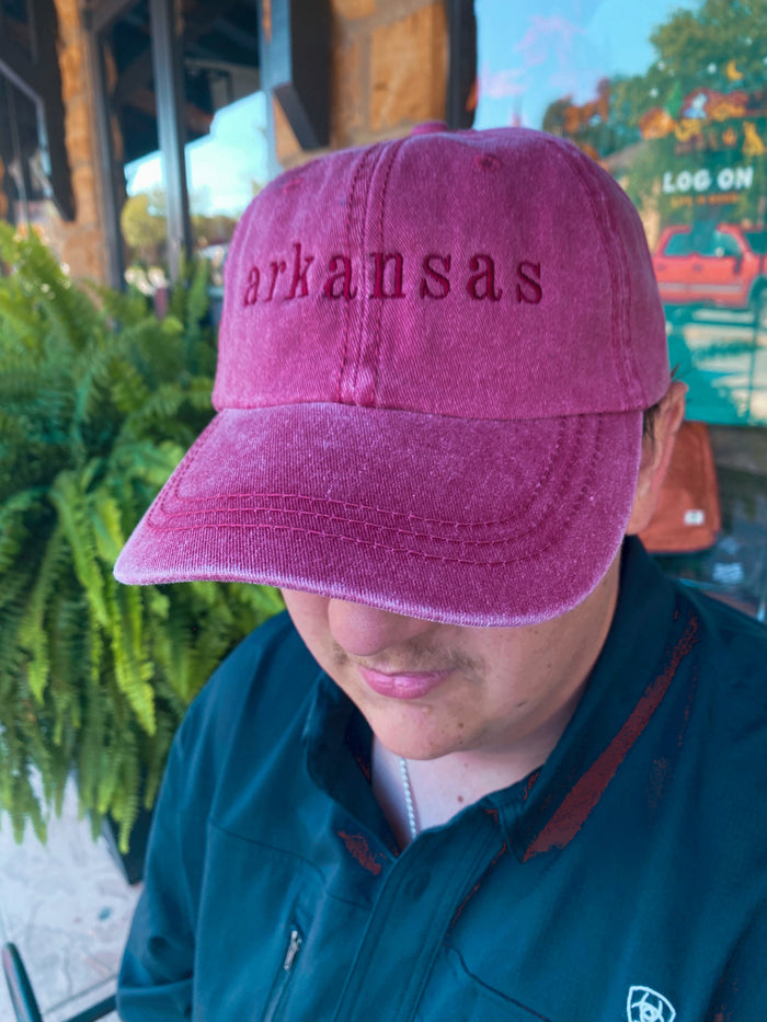 red embroidered Arkansas cap being worn outside in front of a green fern plant