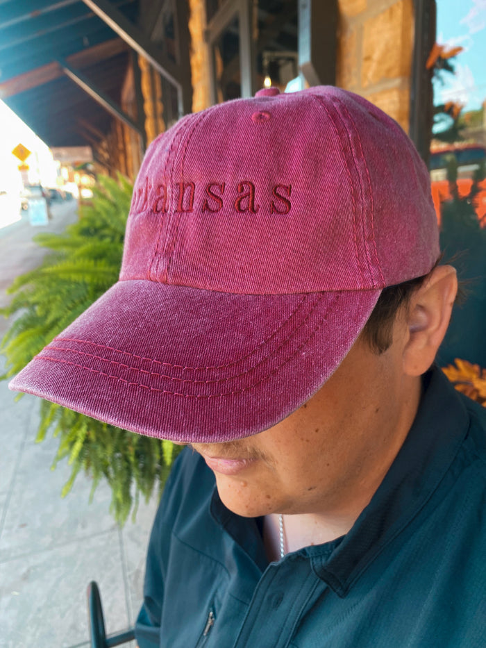 red embroidered Arkansas cap being worn outside in front of a green fern plant