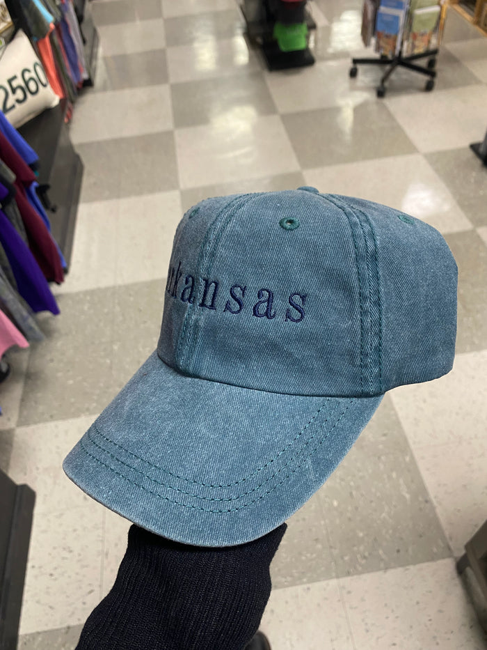 blue jean Arkansas embroidered hat being held against concrete floor