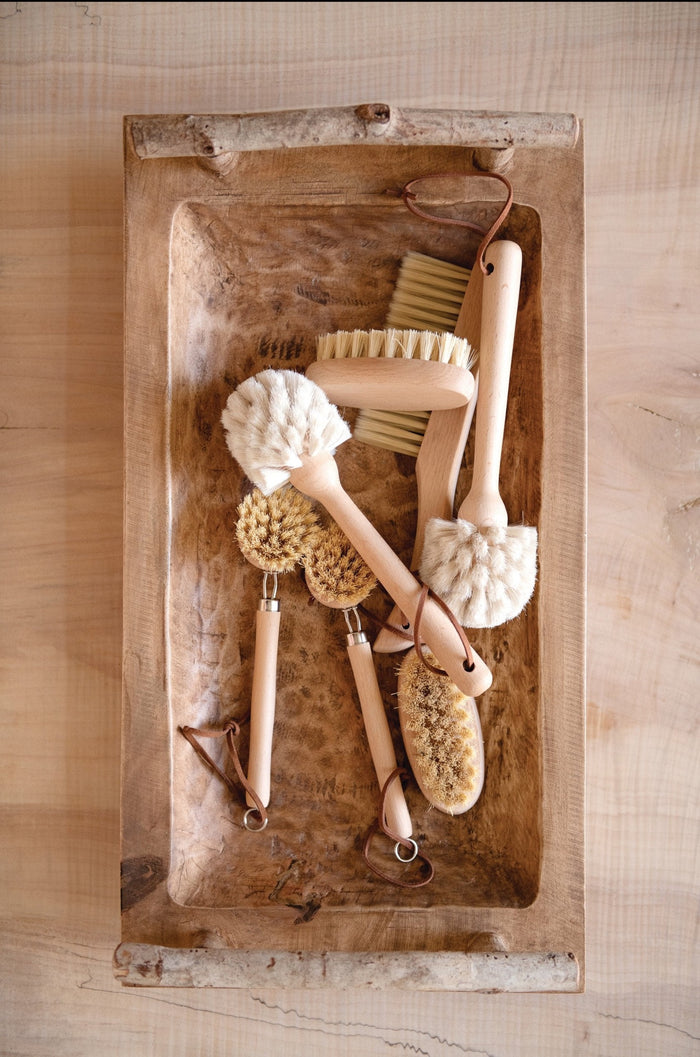 scrubbing brushes in a wood carved bowl on a wooden table