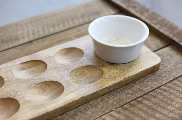 White ceramic cup on a wooden tray with circular indentations
