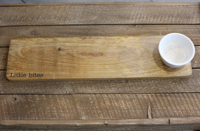 Wooden board with 'Little bites' engraving and a white bowl on a wooden surface
