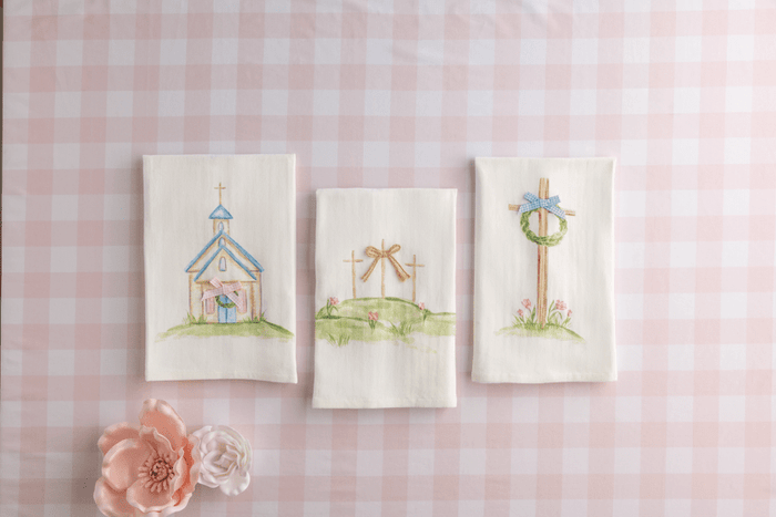 Three embroidered pictures of a church, garden, and cross on a pink checkered background.