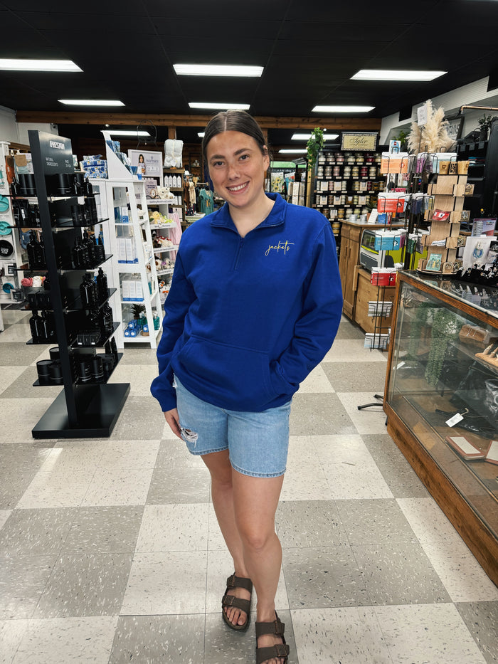 Woman in a blue sweatshirt standing in a store with shelves and products in the background