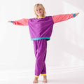Child wearing a colorful outfit with a purple top and pink sleeves on a white background