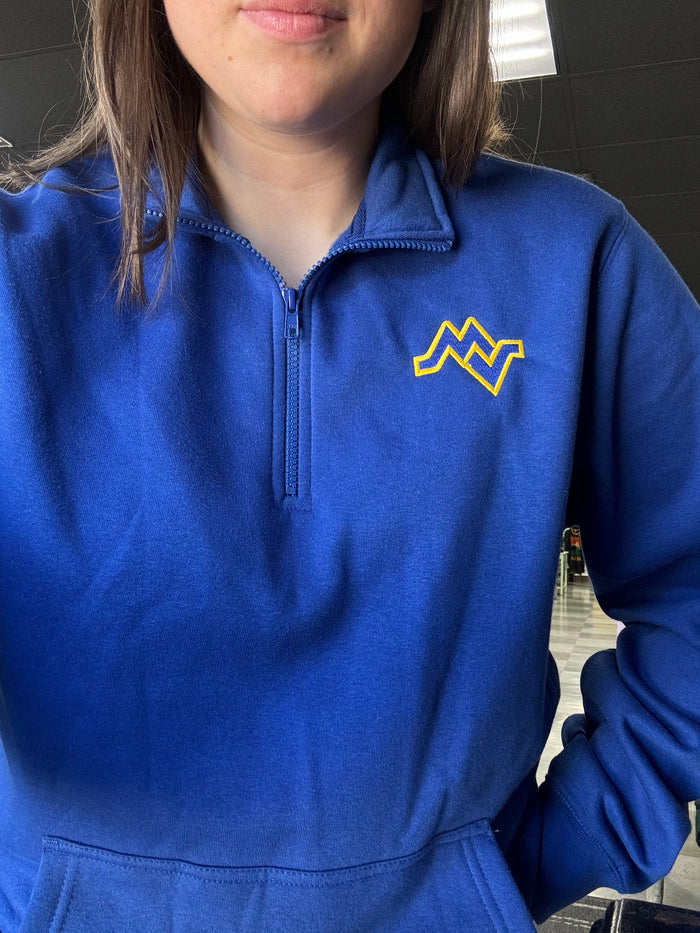 Person wearing a blue jacket with a yellow logo, standing indoors.