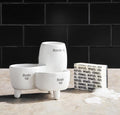 Set of white ceramic containers with text on a wooden surface and black tiled wall background