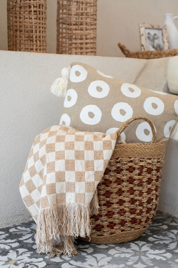 Woven basket with a checkered blanket and decorative pillow on a sofa.